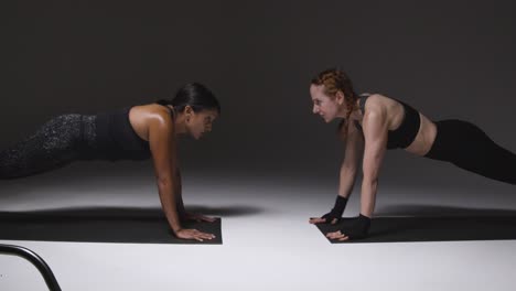 Studio-Shot-Of-Two-Mature-Women-Wearing-Gym-Fitness-Clothing-Doing-Plank-Exercise-Together